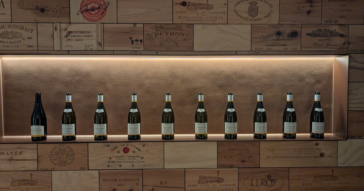 Ten Kumeu River bottles standing in a lit recess set into a wall clad entirely in the printed end panels of wine crates