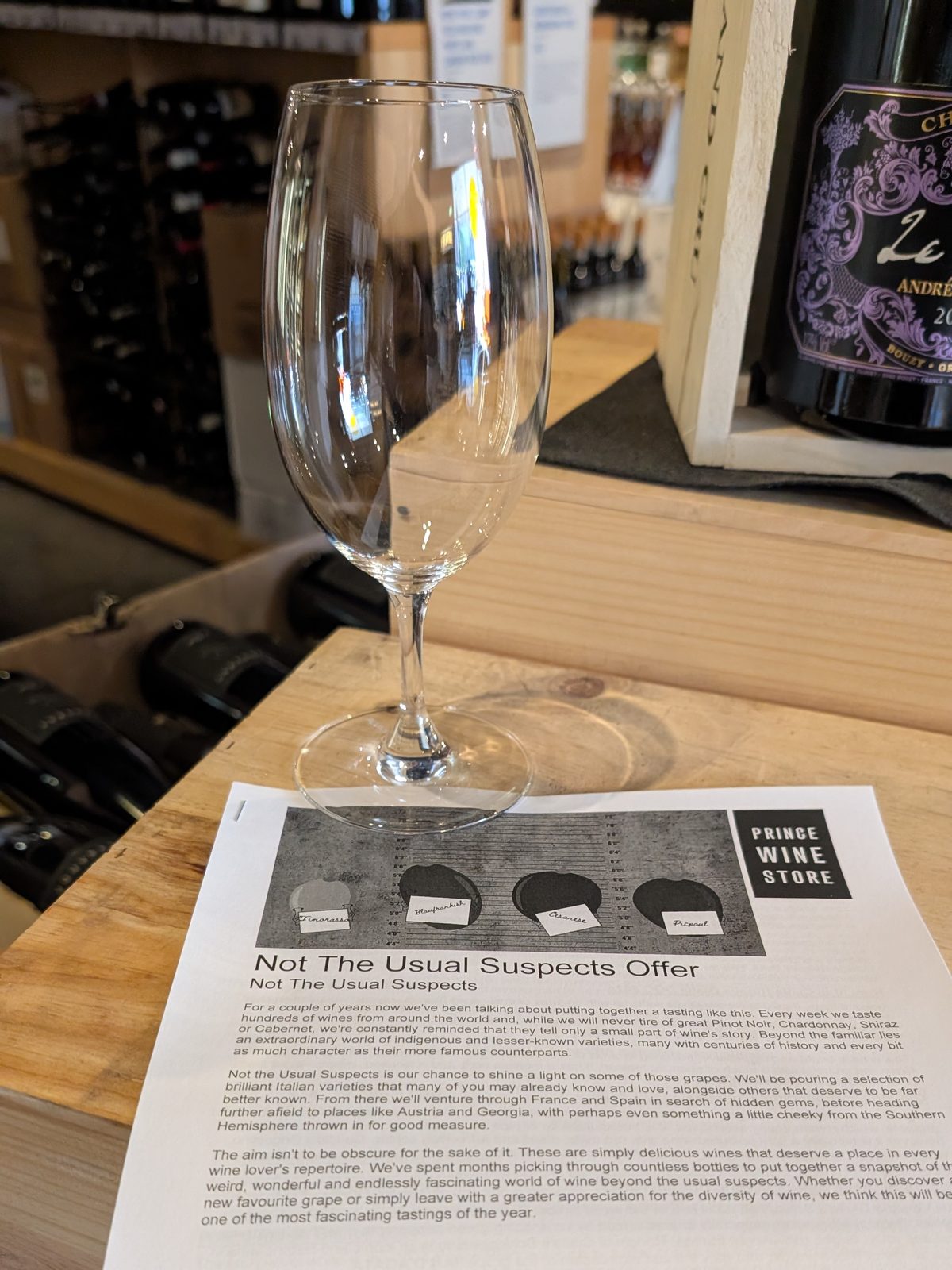 The Not The Usual Suspects tasting sheet on the counter beside an empty tasting glass, its header illustrated with grape names including Timorasso, Blaufränkisch, Cesanese and Picpoul