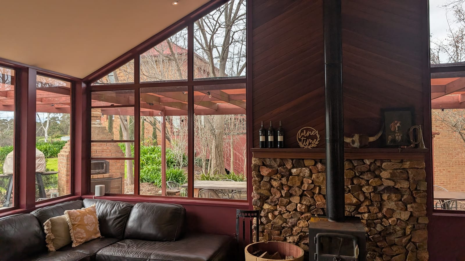 The cellar door lounge, a leather sofa under tall windows looking out to bare winter trees, beside a stone chimney breast and a wood heater