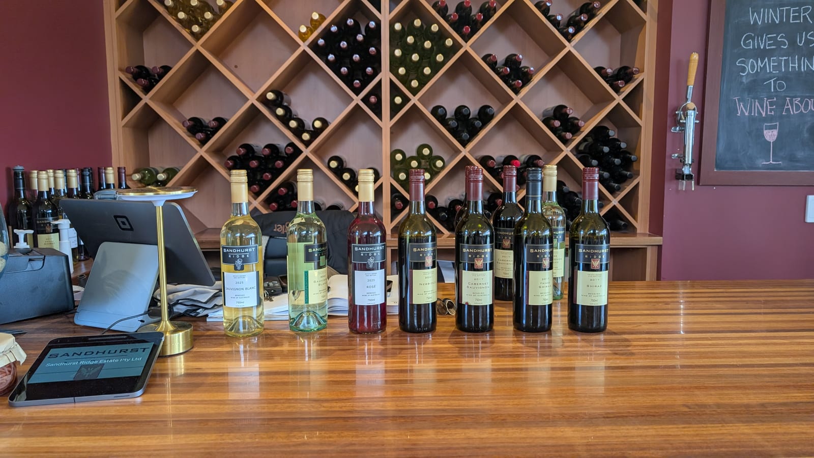 The seven Sandhurst Ridge bottles standing in tasting order along the timber counter, backed by a diamond-latticed wine rack